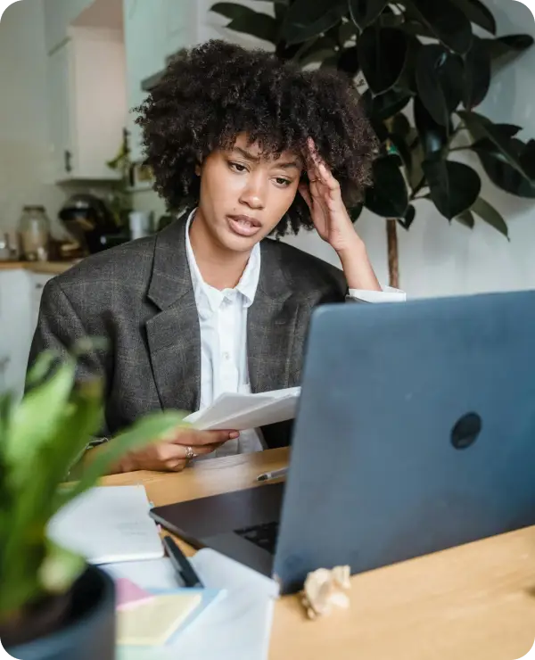 Businesswoman reviewing paperwork while looking at her laptop